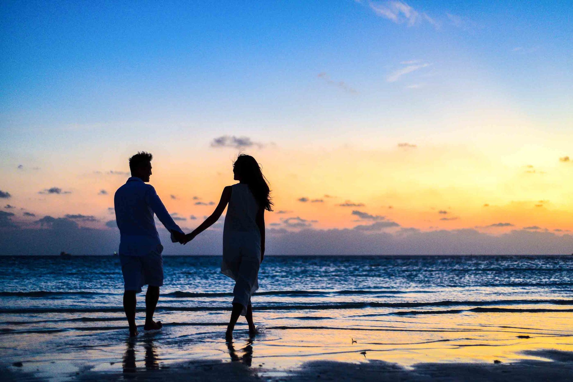 man and woman holding hands walking on seashore during sunrise celebrating after timeshare cancellation. 